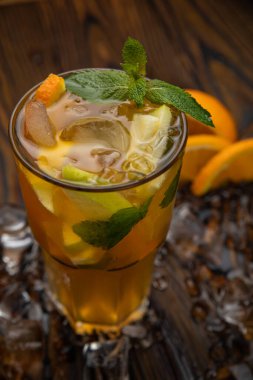 Kahverengi ahşap bir masada elma ve portakallı buzlu çay. Naneyle süslenmiş..