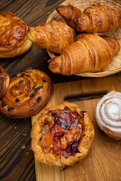 Çeşitli hamur işleri, kruvasanlar, çörekler. Kahverengi ahşap masada.