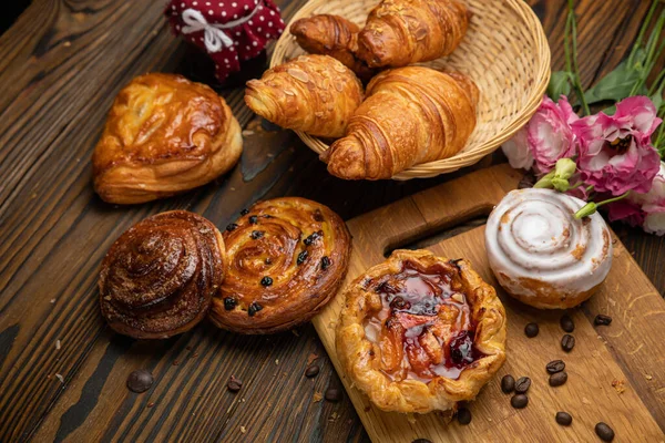 Çeşitli hamur işleri, kruvasanlar, çörekler. Kahverengi ahşap masada.