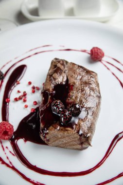 Beyaz tabakta ahududu soslu geyik eti. Beyaz ahşap bir masada.