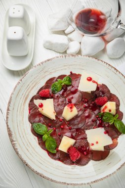 Parmesan ve nar soslu dana carpaccio. Beyaz ahşap bir masada.