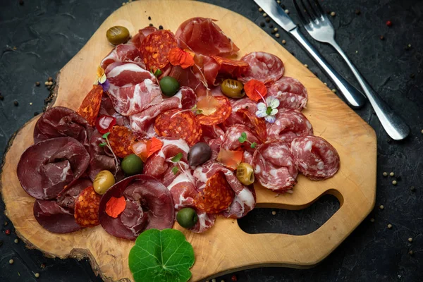 Tütsülenmiş et, sosis, parma, ahşap bir tahtada jamon ve koyu beton bir masa..