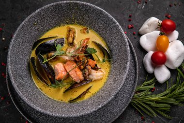 Tayland çorbası, deniz ürünleri, karides, somon. Koyu beton bir masada gri, derin bir taş tabakta servis edilmiş.