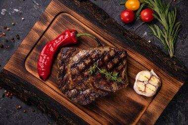 Amerikan sulu bifteği, baharatlar, domates ve ızgara sebzelerle birlikte. Siyah bir masada. 