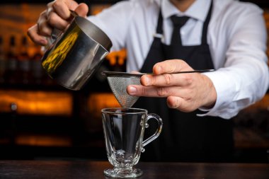 Siyah önlüklü, gülümseyen genç bir barmen sıcak şarap hazırlar.