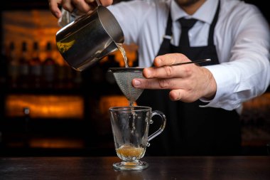 Siyah önlüklü, gülümseyen genç bir barmen sıcak şarap hazırlar.