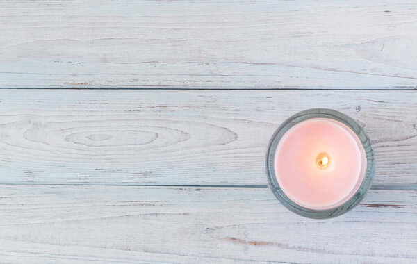 Wooden background from boards of blue and white color with a burning pink candle in the lower corner. The texture of the boards. View top.