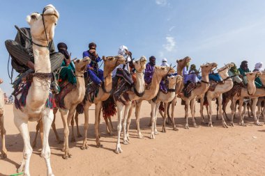 Tuareg people in traditional clothes sitting on camels in Sahara desert