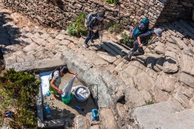 Pokhara, Nepal : Woman washing clothes and hikers in mountain village 
