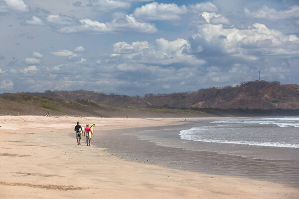 Surfers walk along sandy beach