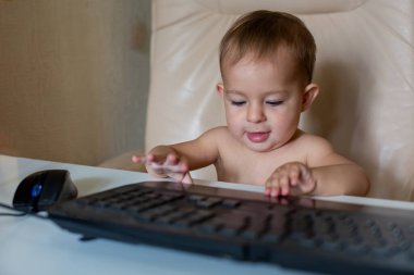 Şirin küçük bebek ofis sandalyesinde oturuyor ve siyah klavye koyuyor, yakın plan, yumuşak odaklı, arka plan bulanık