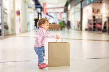 Kara Cuma konsepti, çocuklarla alışveriş, doğa dostu alışveriş. Küçük tatlı kız alışveriş için büyük el işi kağıt torbaları al. yakın plan, yumuşak odak, arka plan dükkanları, yan görünüm.