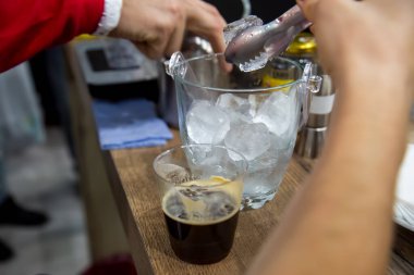 Elinde maşa olan bir el vazodan buz alır ve plastik bardağa yeni demlenmiş kahve koyar. yakın plan, yumuşak odak, bulanık arkaplan