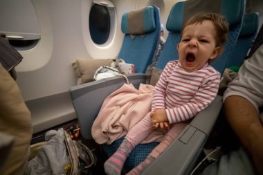 Küçük tatlı uykucu bebek bir uçak koltuğunda oturuyor ve uzun bir uçuşta rahat bir uykudan sonra esniyor.