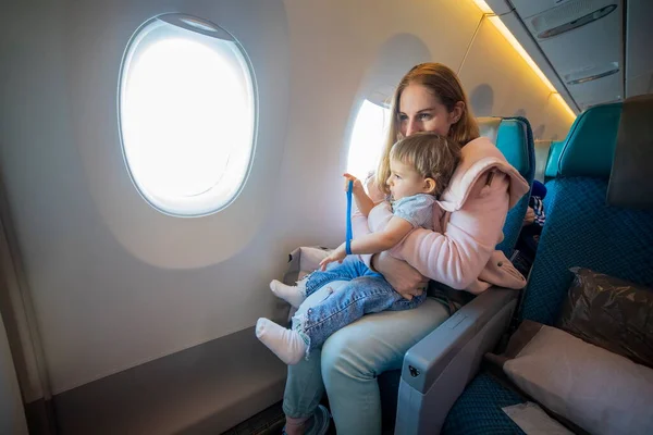 Aile tatili kavramı. Genç ve güzel bir anne bir uçak koltuğunda oturur ve kucağında küçük şirin bir çocuğa sarılır..