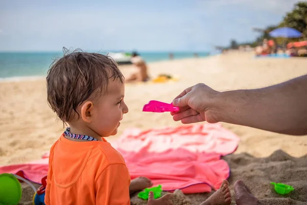 Koncepcja otwierania lotów między krajami, zakończenia kwarantanny pandemicznej planety świata. Mały uroczy maluch siedzi na plaży, patrzy na zabawkowy samolot trzymany przez rodzica i śmieje się szczęśliwy. — Zdjęcie stockowe