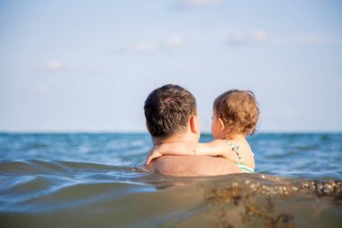 Aile tatili kavramı. Baba deniz suyunda küçük tatlı bir kız çocuğu tutuyor ve ufuk çizgisine bakıyor.