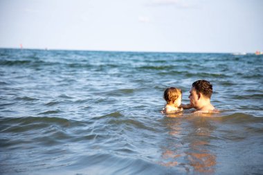 Baba, küçük kızına sıcak bir denizin suyunda yüzmeyi öğretiyor.