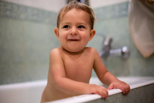 Concept de bonheur. heureux petit bébé mignon se tenir dans un bain à la maison sourit. en arrière-plan une salle de bain verte en flou. gros plan, mise au point douce — Photo