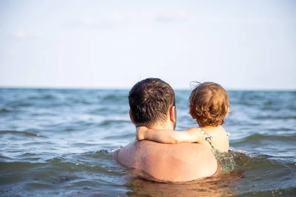 父と小さなかわいい幼児の娘は海の水の中に立って地平線を見ています。後景 — ストック写真