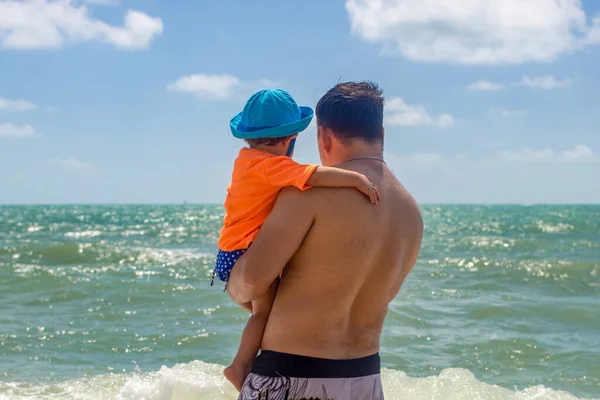 父の日。父は海の波を背景に腕の中で幼児を抱えています — ストック写真