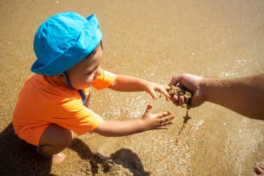 Mavi şapkalı şirin çocuk deniz sahilinde babasıyla kum oynuyor. Kapat..