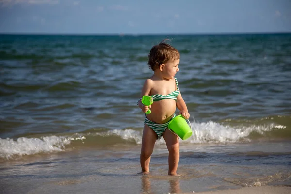 Mały wesoły szczęśliwy chłopiec bawi się w falach morza z wiadrem i łopatą — Zdjęcie stockowe