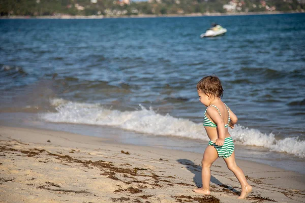 Mały słodkie dziecko biegnie wzdłuż plaży morskiej w słoneczny ciepły dzień — Zdjęcie stockowe