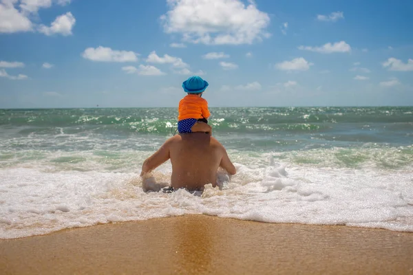Festa dei padri. papà con un bambino sulle spalle giocare sulla riva del mare vista posteriore — Foto Stock