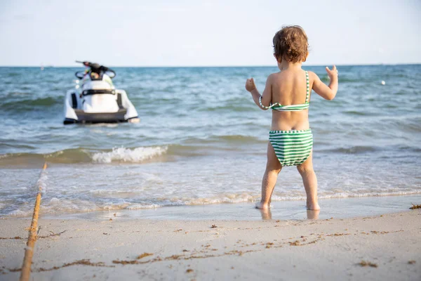 Słodkie dziecko maluch stoi na brzegu i patrząc na morze widok z tyłu. — Zdjęcie stockowe