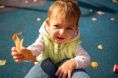Sonbaharda kuru sarı meşe yaprağı üzerinde çalışan bir yaşında tatlı bir kız. Yakın plan. Sonbaharda çocuk portresi