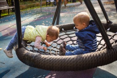 Sonbahar parkında bir parkta sallanan bir hamakta bir kız ve bir oğlan neşeyle oynuyorlar.