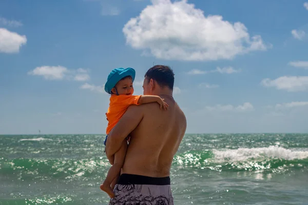 dad hugs toddler baby in his arms on the background of the sea