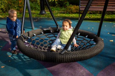 Sonbahar parkında bir parkta sallanan bir hamakta bir kız ve bir oğlan neşeyle oynuyorlar.