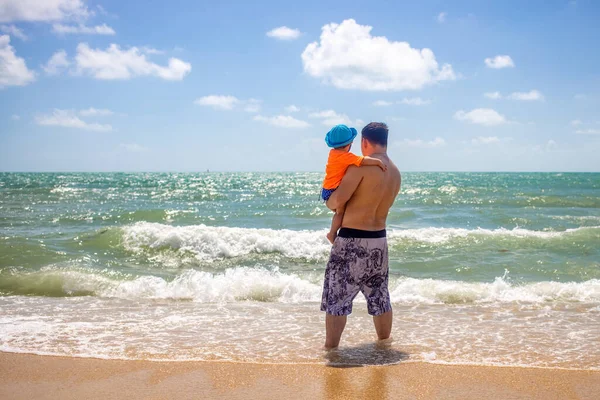 父は赤ん坊を抱いて砂浜に立つ波を見て — ストック写真