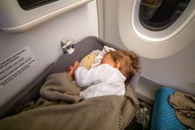 Küçük iki yaşında bir kız bebek uçakta beşiğinde uyur.