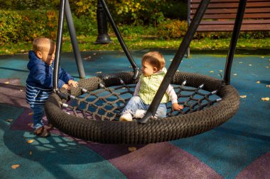 Sonbahar parkında bir parkta sallanan bir hamakta bir kız ve bir oğlan neşeyle oynuyorlar.