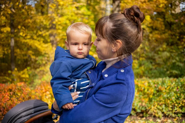 Retrato de una joven y hermosa madre sostiene a un niño en sus brazos y lo besa suavemente en el parque de otoño. madres amor concepto — Foto de Stock
