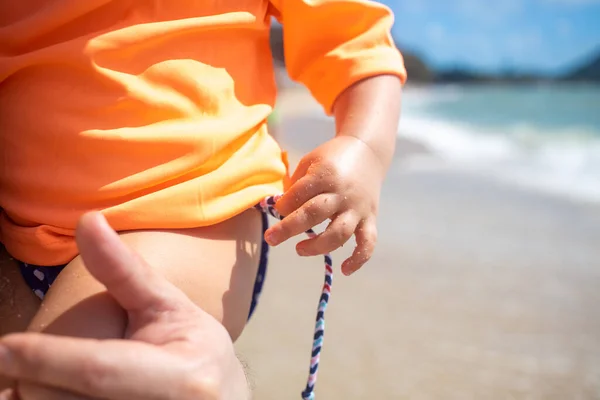 close-up childrens hand pulls the rope of a swimsuit sitting with dad in his arms