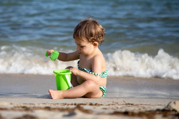 Mały radosny szczęśliwy dzieciak bawiący się wiadro i gałka siedzi na brzegu morza — Zdjęcie stockowe