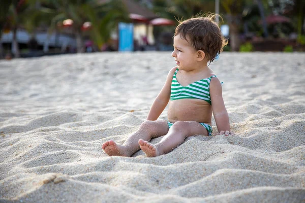 Urocza dziewczyna w stroju kąpielowym siedzi na piaszczystej plaży w słońcu. — Zdjęcie stockowe