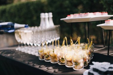 Meyveli bardaklar, şampanyalı bardaklar şampanyalı şişeler, kanepeli raflar. Resepsiyon, yemek servisi. Masa siyah bir masa örtüsüyle kaplı..