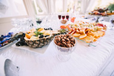 Fındık, ananaslı ve tabakta çeşitli meyveler. Resepsiyon, yemek servisi. Masa beyaz bir masa örtüsüyle kaplıdır..