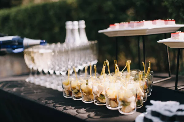 Meyveli bardaklar, şampanyalı bardaklar şampanyalı şişeler, kanepeli raflar. Resepsiyon, yemek servisi. Masa siyah bir masa örtüsüyle kaplı..