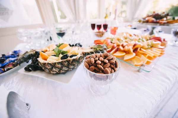 Fındık, ananaslı ve tabakta çeşitli meyveler. Resepsiyon, yemek servisi. Masa beyaz bir masa örtüsüyle kaplıdır..