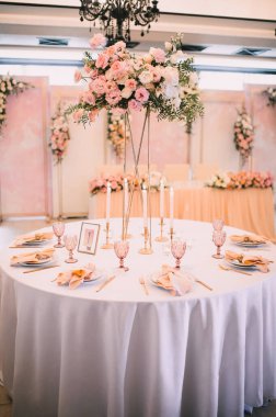 Ziyafet, restoran. Masa ayarı. Altın kenarlı beyaz tabaklar, altın çatal bıçak takımı, gözlük. Altın yüzüklü şeftali renkli peçete. Şeftali pembesi çiçek aranjmanları. Altın mum tutacaklarında ince ince ince inceler.