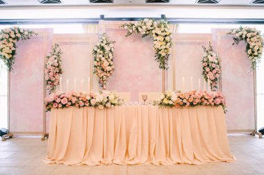 Ziyafet, restoran. Masa ayarı. Masanın üzerinde pembe bir masa örtüsü var. Presidium, yeni evlilerin masası. Masanın üzerinde bir masa örtüsü var. Şeftali pembesi renklerinde çiçek aranjmanları. Uzun mumlar.