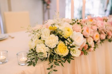 Ziyafet, restoran. Masa ayarı. Masanın üzerinde pembe bir masa örtüsü var. Presidium, yeni evlilerin masası. Masanın üzerinde bir masa örtüsü var. Şeftali pembesi renklerinde çiçek aranjmanları. Uzun mumlar.
