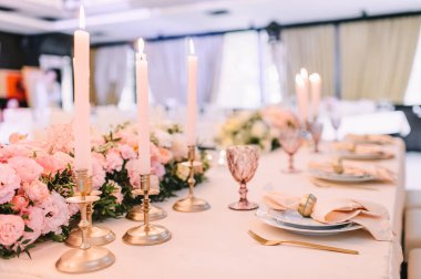 Ziyafet, restoran. Masa ayarı. Şeftali pembesi çiçek aranjmanları. Altın mum tutacaklarında ince ince ince inceler.