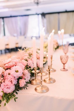 Ziyafet, restoran. Masa ayarı. Şeftali pembesi çiçek aranjmanları. Altın mum tutacaklarında ince ince ince inceler.